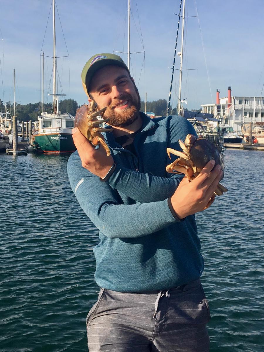 Andrew Jensen holding two crabs while standing at a boat dock.