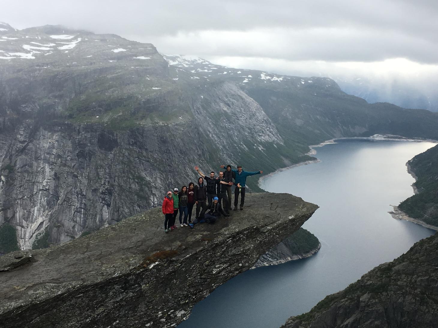 A group of people standing on a cliffside overlooking a river.