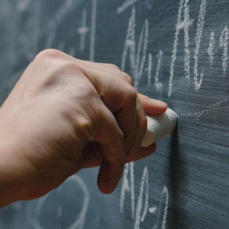 Photo of a hand writing math equations on a chalk board