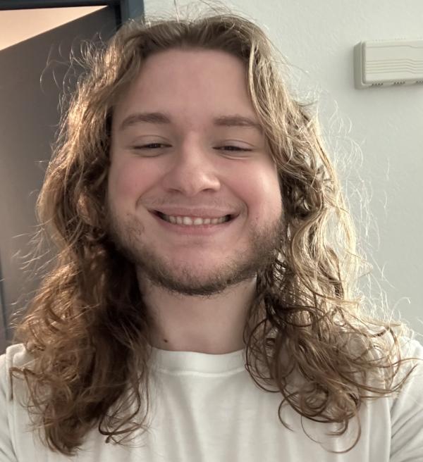 A man with long curly hair and a short beard wearing a white shirt