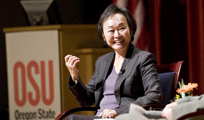 Peggy Cherng sits in a suit on stage giving a talk at an OSU event.